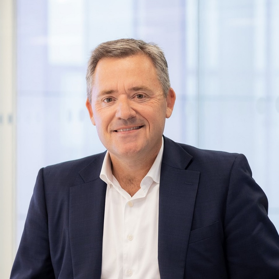 Person in a suit smiling in a bright office setting.