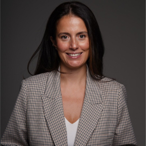 Person smiling in a checkered blazer against a dark background.