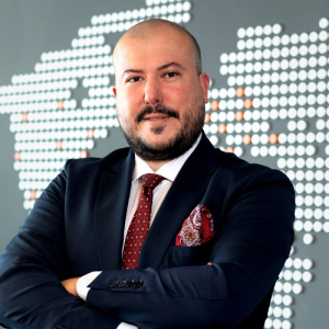 Person in a suit with crossed arms stands in front of a stylized map background.