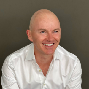 Person smiling, wearing a white shirt against a plain background.