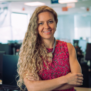 Person with long curly hair smiling in an office setting.