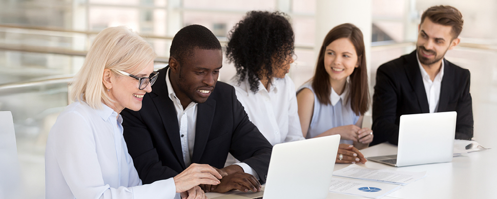 A diverse group of professionals working together on laptops at a bright, modern office table.