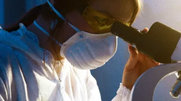 Scientist in a lab coat examines a sample under a microscope.