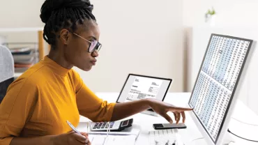 Person working at a desk with two computer monitors, analyzing data on a screen.