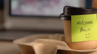 Coffee cup with 'Welcome Back' note and a smiley face.