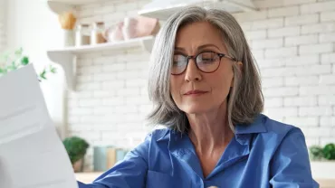 Person in blue shirt reading a document in a bright kitchen.