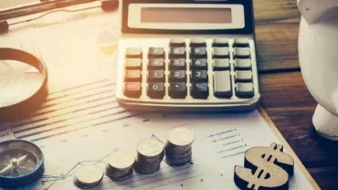 Calculator, coins, magnifying glass, and piggy bank on financial documents.