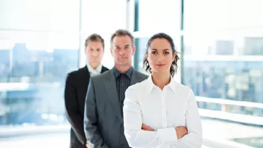 Three professionals in a modern office, with a woman leading the group.