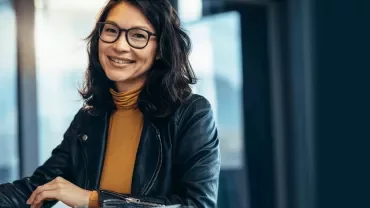 Person with glasses smiling and using a laptop indoors.