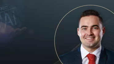 A professional portrait of a smiling man in a suit and red tie, overlaid on a dark background featuring subtle graphic lines and a futuristic hologram of "AI" in a cube held by a hand.