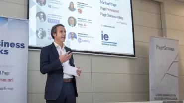 a man talking in a conference with a screen in the background