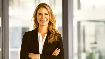 Person in a business suit smiling with arms crossed indoors.