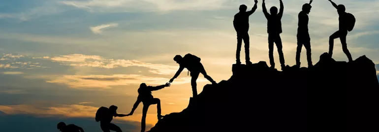 Silhouette of climbers helping each other on a mountain at sunset.