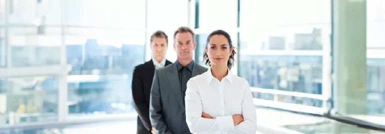 Three professionals in a modern office, with a woman leading the group.