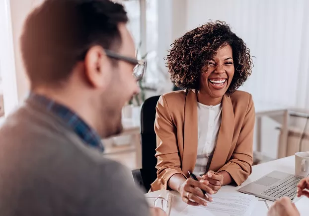 A smiling businesswoman holding a pen during a meeting with a colleague in an office setting